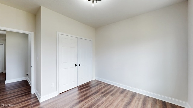 unfurnished bedroom with a closet, dark wood finished floors, and baseboards