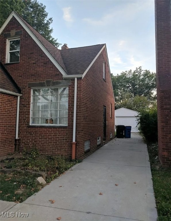 view of side of home featuring an outbuilding, brick siding, a chimney, and a detached garage