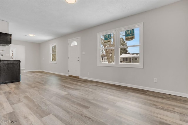 unfurnished living room featuring light wood finished floors and baseboards