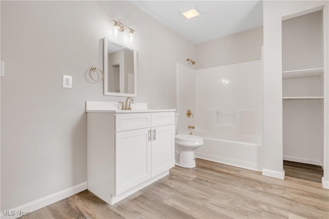 bathroom with baseboards, toilet, shower / tub combination, wood finished floors, and vanity