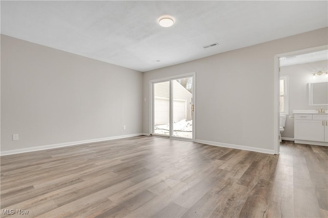 empty room with baseboards, a sink, visible vents, and light wood-style floors