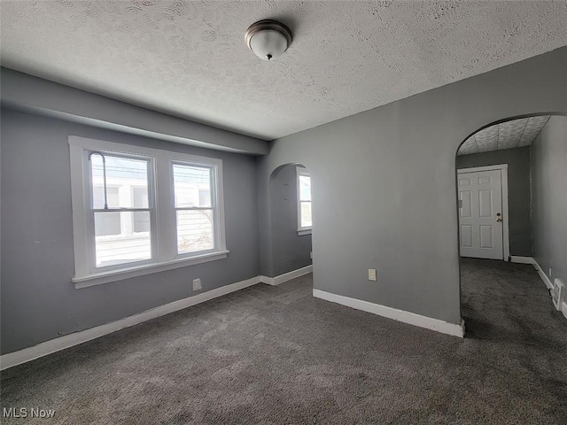 spare room with arched walkways, baseboards, a textured ceiling, and dark colored carpet