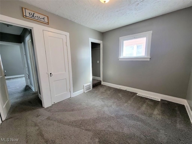 unfurnished bedroom featuring a textured ceiling, dark colored carpet, visible vents, and baseboards