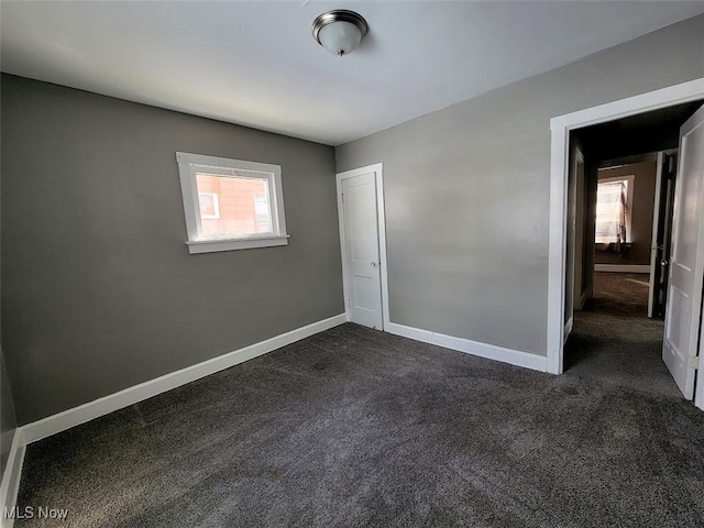 unfurnished bedroom with baseboards and dark carpet