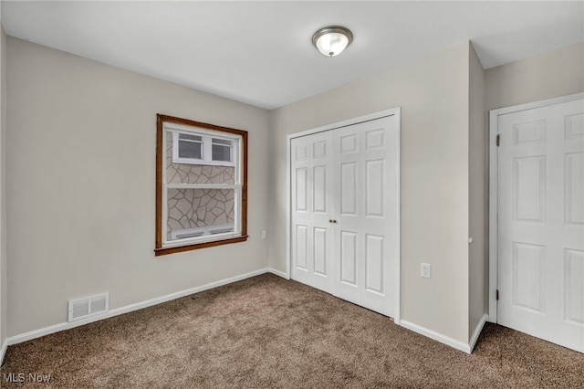 unfurnished bedroom with dark colored carpet, a closet, visible vents, and baseboards