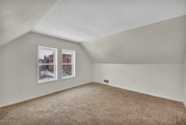 additional living space featuring baseboards, visible vents, vaulted ceiling, a textured ceiling, and carpet floors