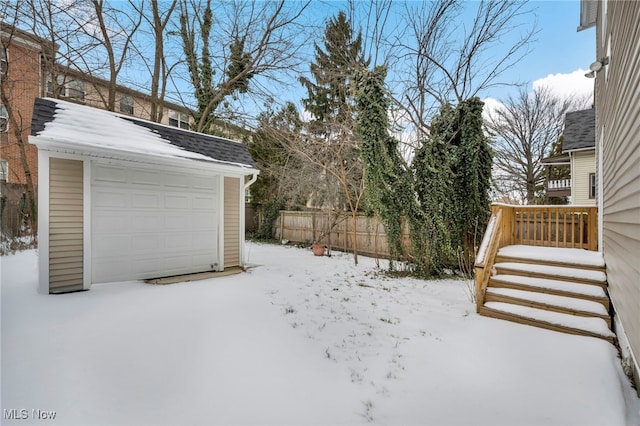 snowy yard featuring a garage, fence, and an outdoor structure