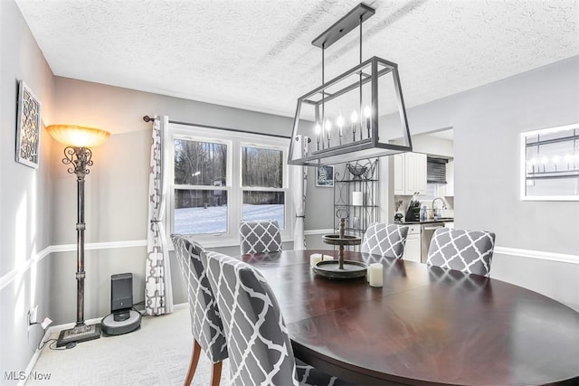 carpeted dining room featuring a textured ceiling, a sink, and baseboards