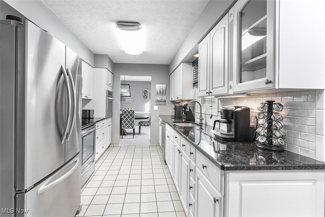 kitchen with appliances with stainless steel finishes, white cabinetry, glass insert cabinets, and a sink