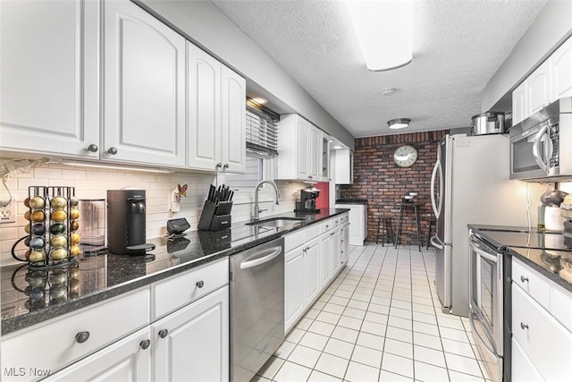 kitchen featuring light tile patterned floors, white cabinets, appliances with stainless steel finishes, dark stone countertops, and a sink