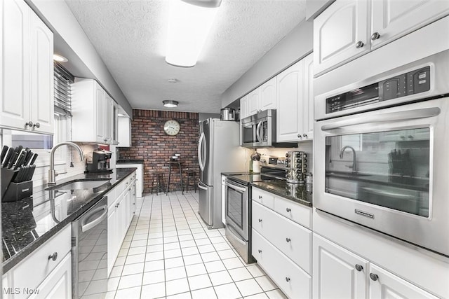 kitchen featuring light tile patterned floors, brick wall, stainless steel appliances, white cabinetry, and a sink