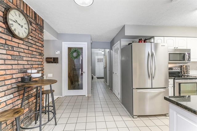 kitchen featuring appliances with stainless steel finishes, dark stone counters, white cabinets, and light tile patterned flooring