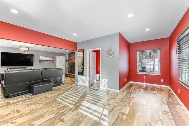 unfurnished living room featuring light wood-type flooring, a brick fireplace, and baseboards