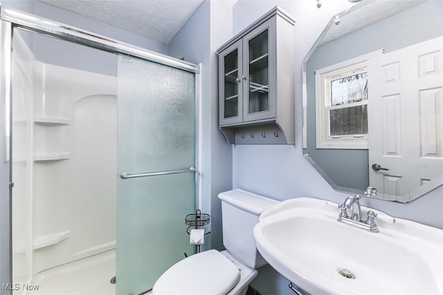 bathroom with a textured ceiling, a stall shower, a sink, and toilet