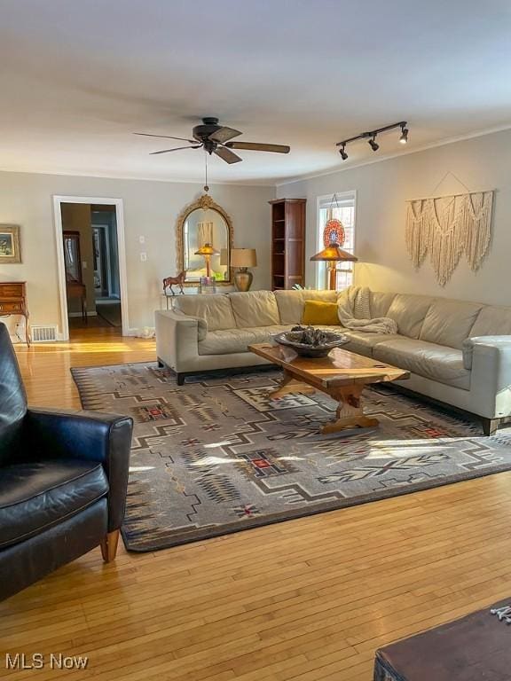 living area featuring rail lighting, visible vents, ornamental molding, ceiling fan, and hardwood / wood-style floors