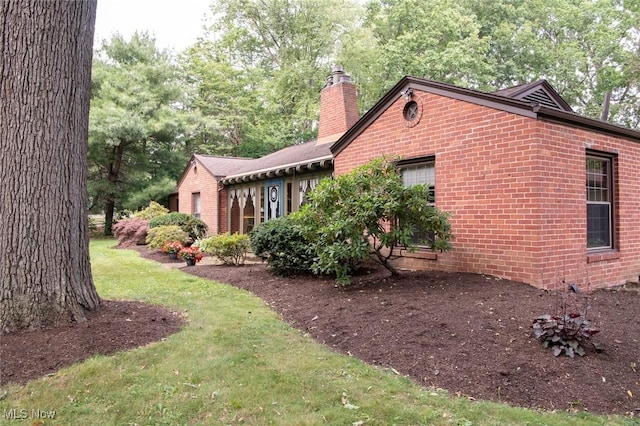 view of side of home with a chimney, a lawn, and brick siding