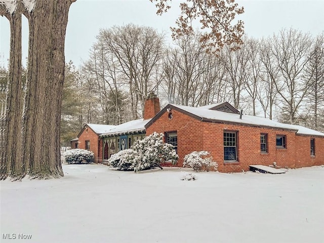 snow covered property featuring a chimney and brick siding