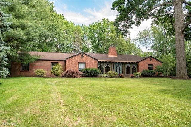 single story home featuring brick siding, a chimney, and a front yard