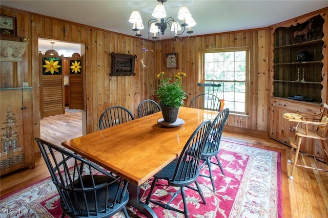 dining room featuring light wood-type flooring, wood walls, a chandelier, and crown molding