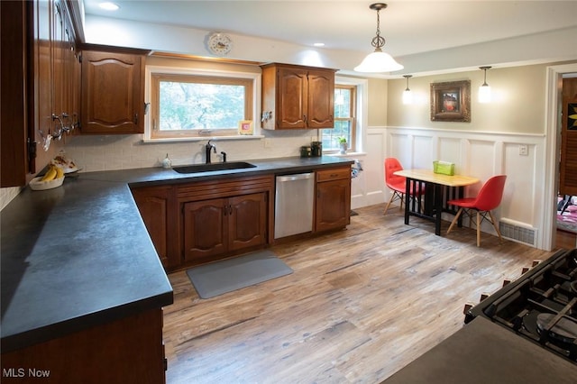 kitchen featuring a wainscoted wall, dark countertops, a sink, light wood-type flooring, and dishwasher