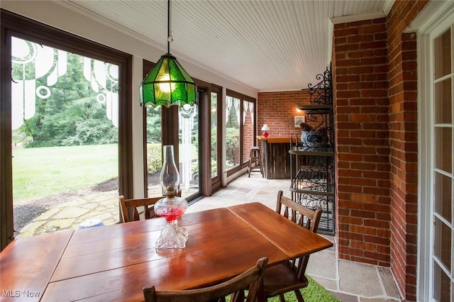 dining space with crown molding, brick wall, and stone tile floors