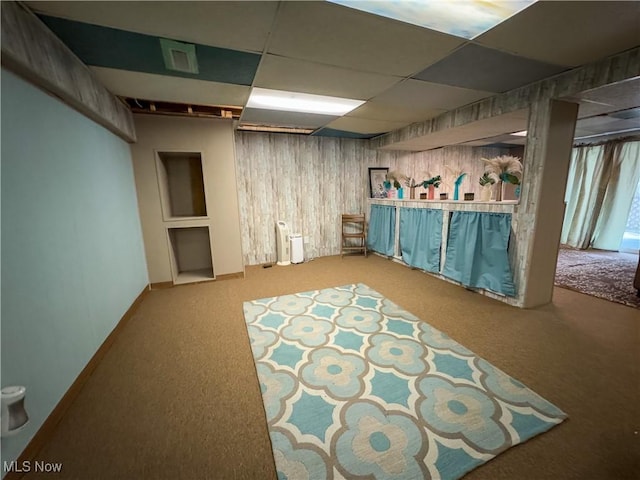 finished basement featuring carpet, wood walls, a drop ceiling, and visible vents