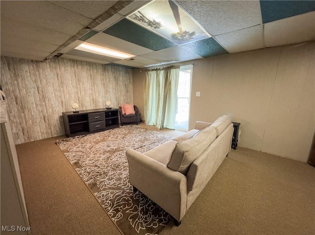 carpeted living area with wood walls and a drop ceiling