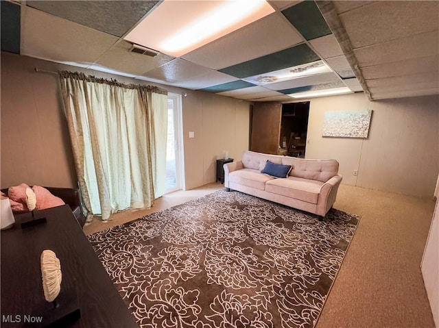 living room with carpet floors, a drop ceiling, visible vents, and wooden walls