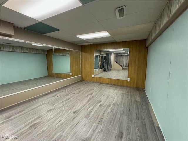 spare room with a paneled ceiling, visible vents, wooden walls, and wood finished floors