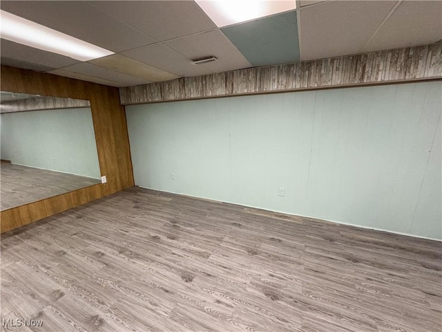 spare room featuring a drop ceiling, wood finished floors, visible vents, and wooden walls