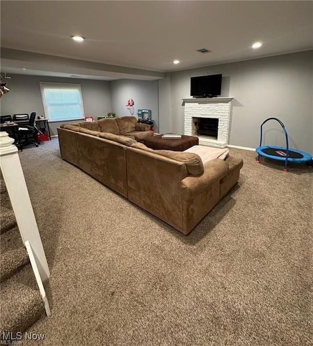 carpeted living room with baseboards, visible vents, a fireplace with raised hearth, stairway, and recessed lighting