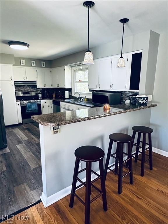 kitchen with stainless steel appliances, hanging light fixtures, decorative backsplash, white cabinets, and a peninsula