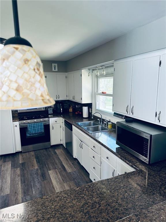 kitchen with stainless steel appliances, a sink, white cabinetry, decorative backsplash, and dark countertops