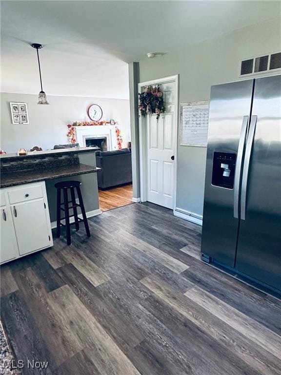 kitchen featuring white cabinets, stainless steel fridge with ice dispenser, dark countertops, dark wood-type flooring, and hanging light fixtures