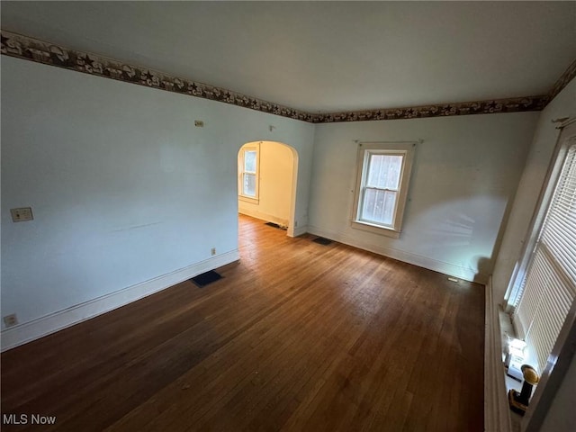 unfurnished room with arched walkways, wood finished floors, visible vents, and baseboards