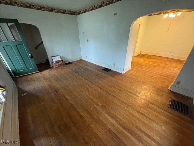 empty room featuring baseboards, visible vents, arched walkways, hardwood / wood-style floors, and stairs