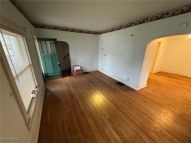 unfurnished room with baseboards, visible vents, arched walkways, and wood finished floors