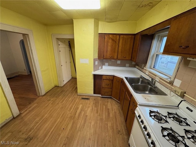 kitchen with light wood-style flooring, a sink, light countertops, brown cabinets, and white gas range