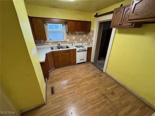 kitchen with a sink, visible vents, light countertops, light wood-type flooring, and white gas range oven