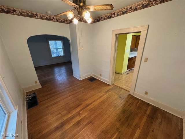 spare room with arched walkways, dark wood-style flooring, a ceiling fan, visible vents, and baseboards