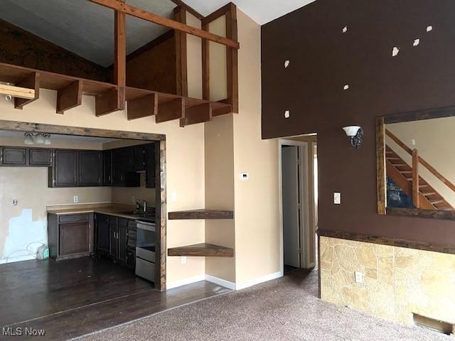 kitchen with high vaulted ceiling, dark colored carpet, and baseboards