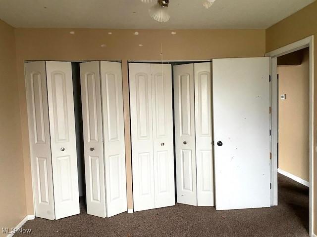 unfurnished bedroom featuring baseboards, dark carpet, and two closets