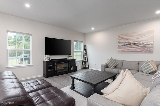 living area with light wood-type flooring, a glass covered fireplace, baseboards, and recessed lighting