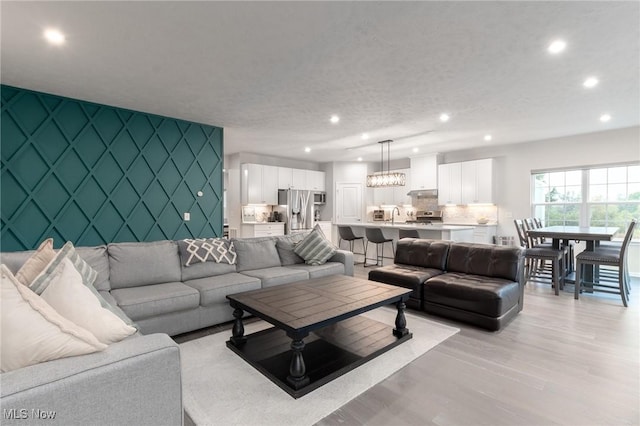 living room featuring light wood finished floors, recessed lighting, an accent wall, a textured ceiling, and wallpapered walls