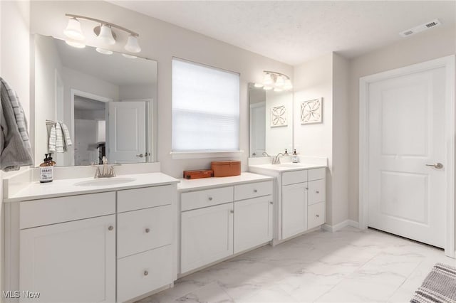 bathroom featuring marble finish floor, two vanities, visible vents, a sink, and a textured ceiling