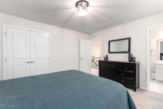 bedroom featuring a textured ceiling, light carpet, visible vents, a closet, and ensuite bath