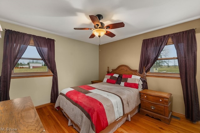 bedroom with light wood-style floors, baseboards, visible vents, and a ceiling fan