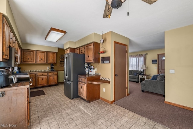 kitchen with brown cabinetry, baseboards, open floor plan, and freestanding refrigerator