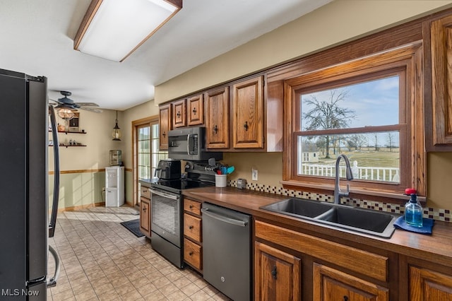 kitchen with brown cabinetry, dark countertops, ceiling fan, stainless steel appliances, and a sink