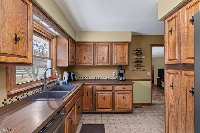 kitchen featuring dark countertops, visible vents, stainless steel dishwasher, brown cabinetry, and a sink